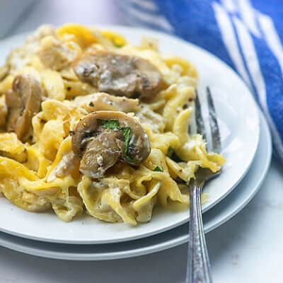 Noodles and mushrooms on a small round white plate with a fork.