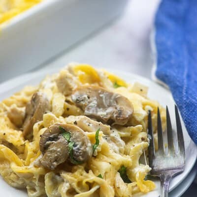 A white plate of noodles topped with mushrooms.