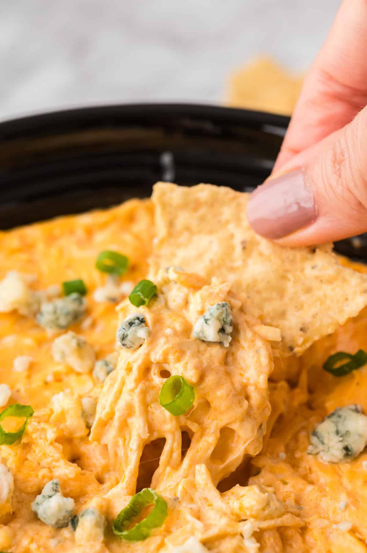 Buffalo dip in a slow cooker topped with chives.