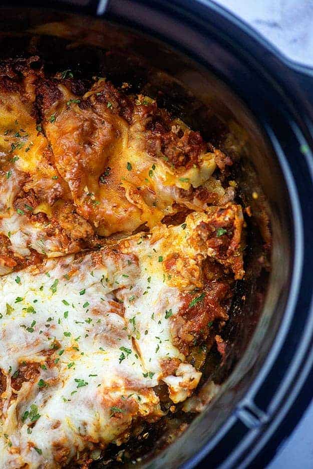 Lasagna in a slow cooker cut into four triangle pieces.