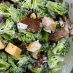 A clear glass bowl of salad with broccoli and bacon pieces.