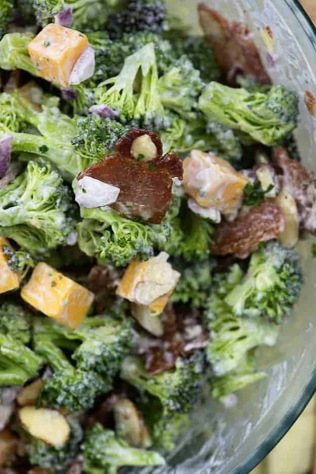 A clear glass bowl of salad with broccoli and bacon pieces.