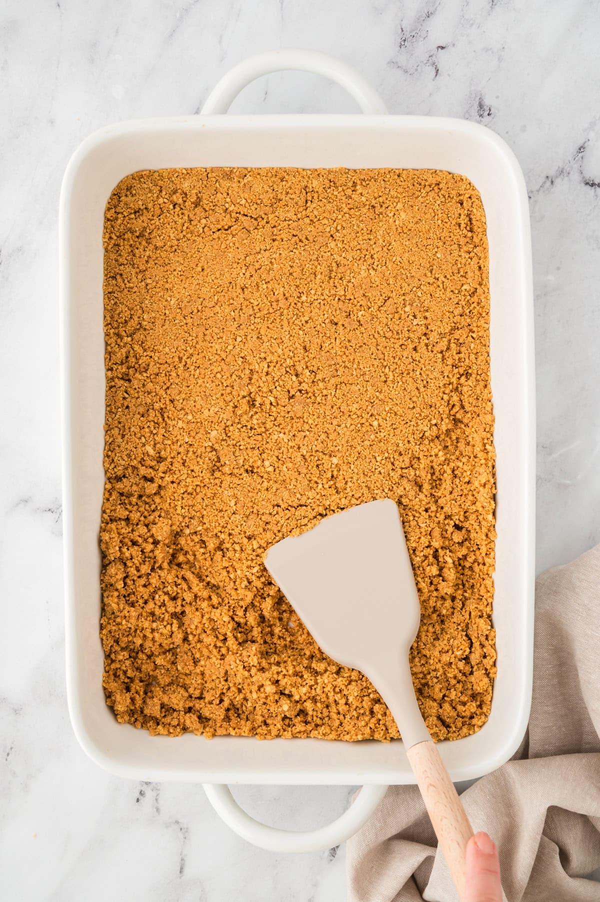 Nutter Butter crust being pressed into 9x13 baking dish.