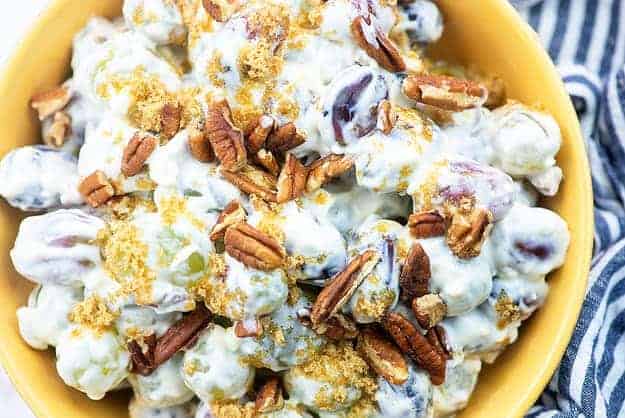 creamy grape salad in yellow bowl with blue striped napkin