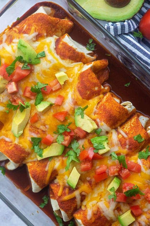 ground beef enchiladas in glass baking dish topped with tomato, avocado, and cilantro