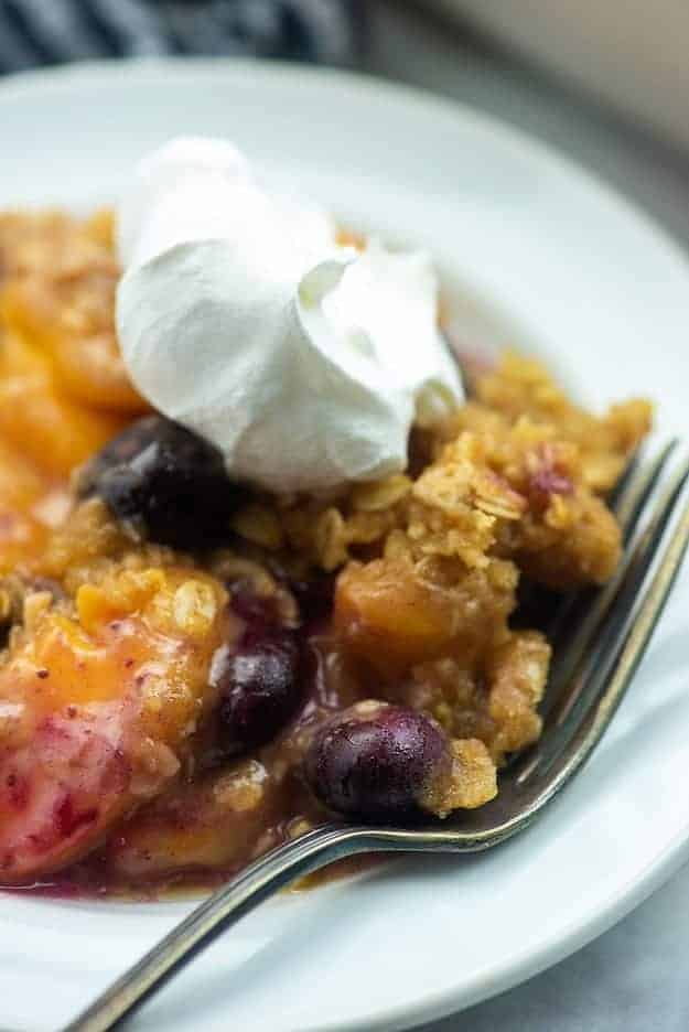 fruit crisp on white plate with whipped cream