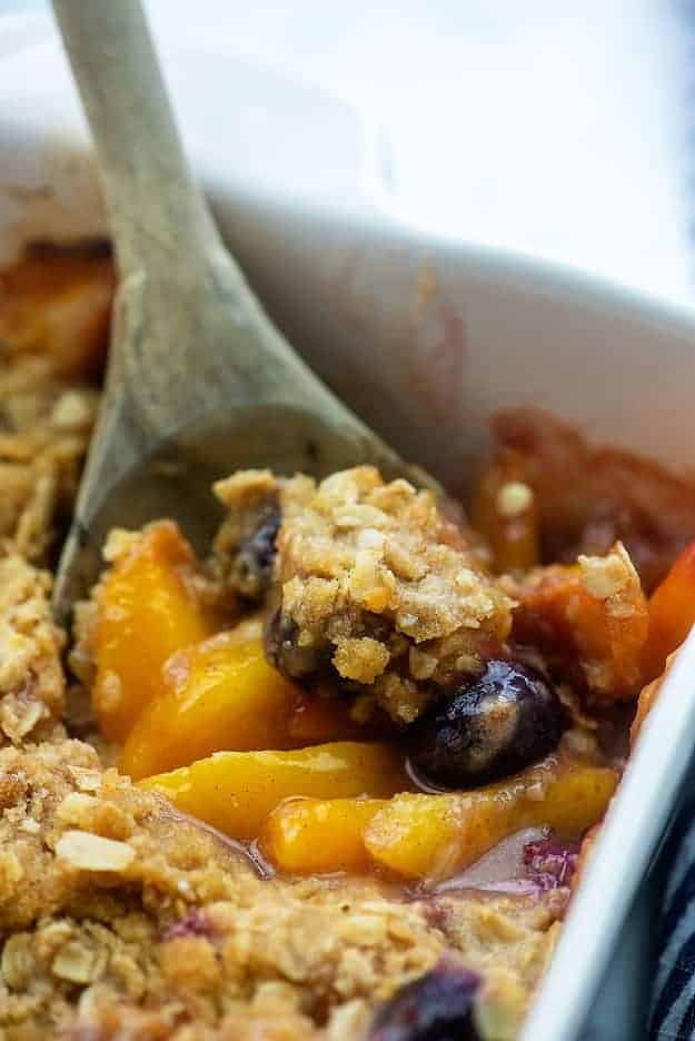 A close up of a white baking dish with peaches and blueberries.