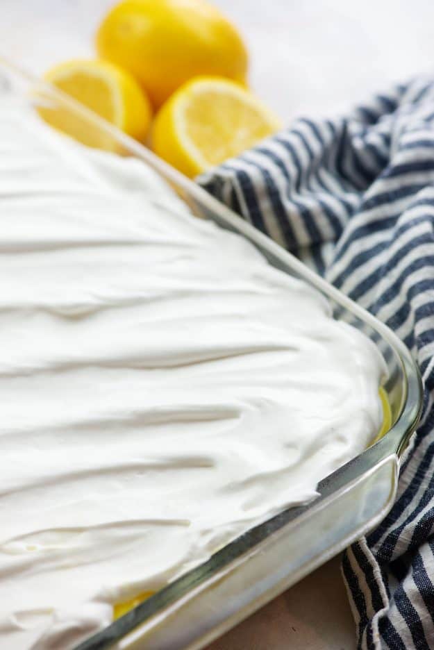 cool whip topping over lemon dessert in glass pan with blue napkin