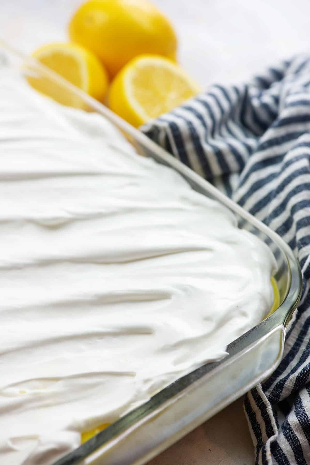 cool whip topping over lemon dessert in glass pan with blue napkin