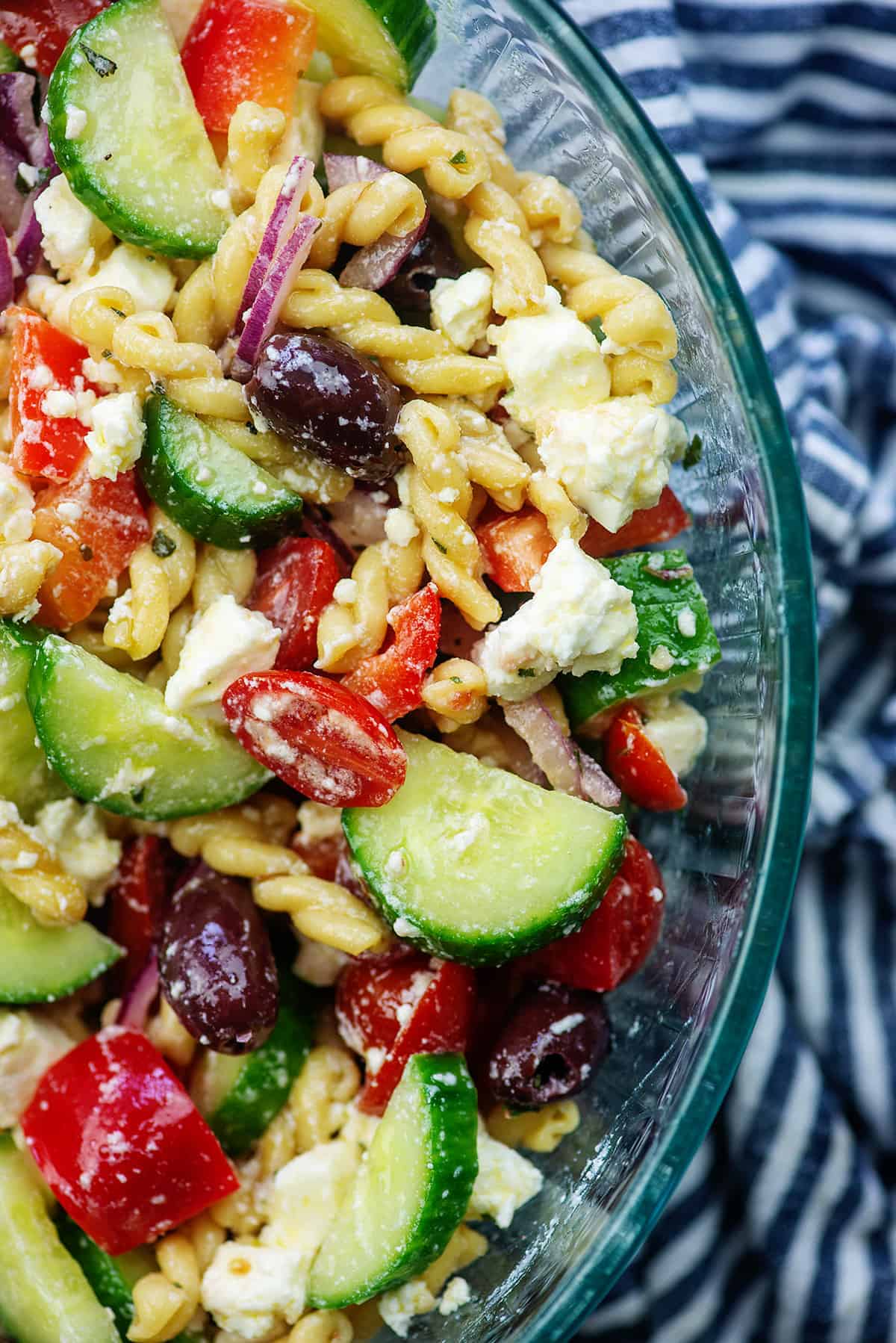 pasta salad recipe with fresh cucumbers, tomatoes, and onions in glass bowl