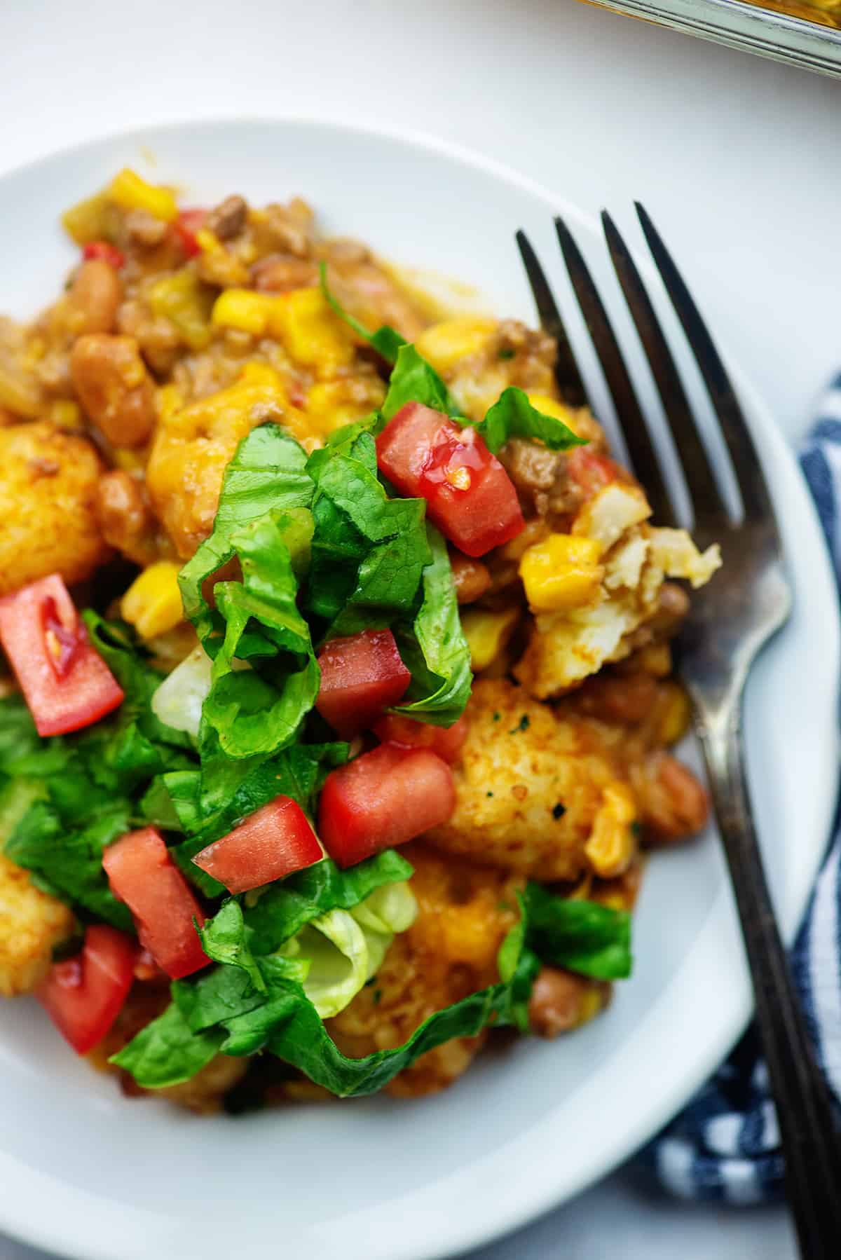 tater tot casserole with lettuce and tomato on white plate