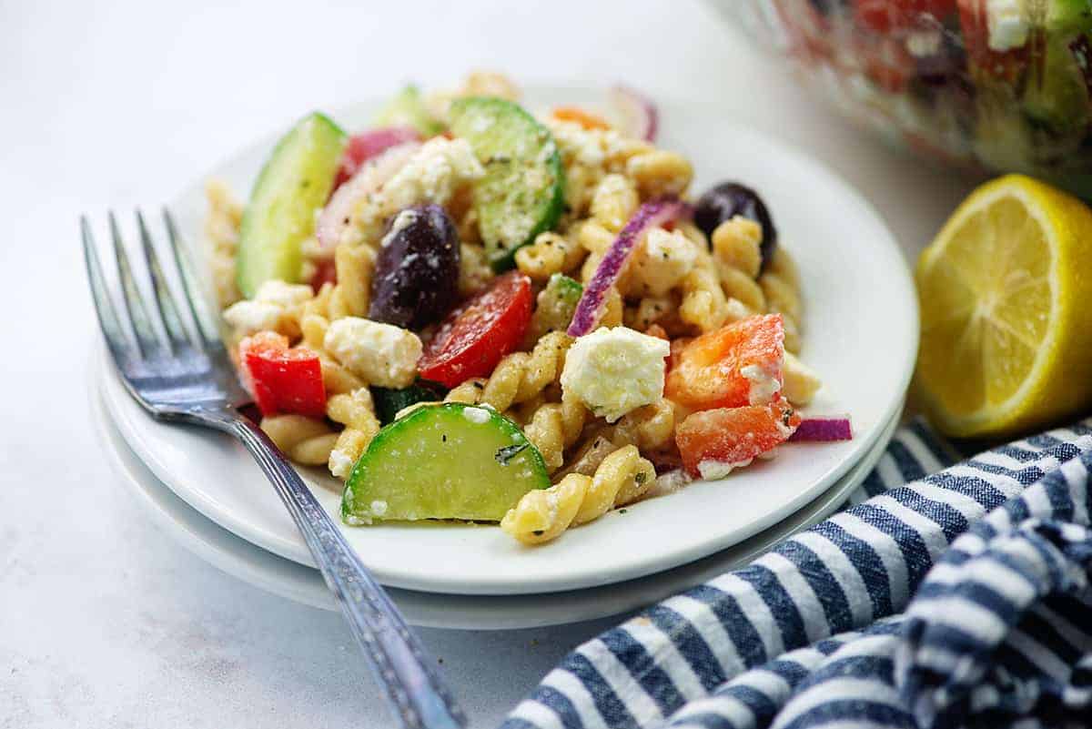 pasta salad on white plate with blue napkin and a lemon