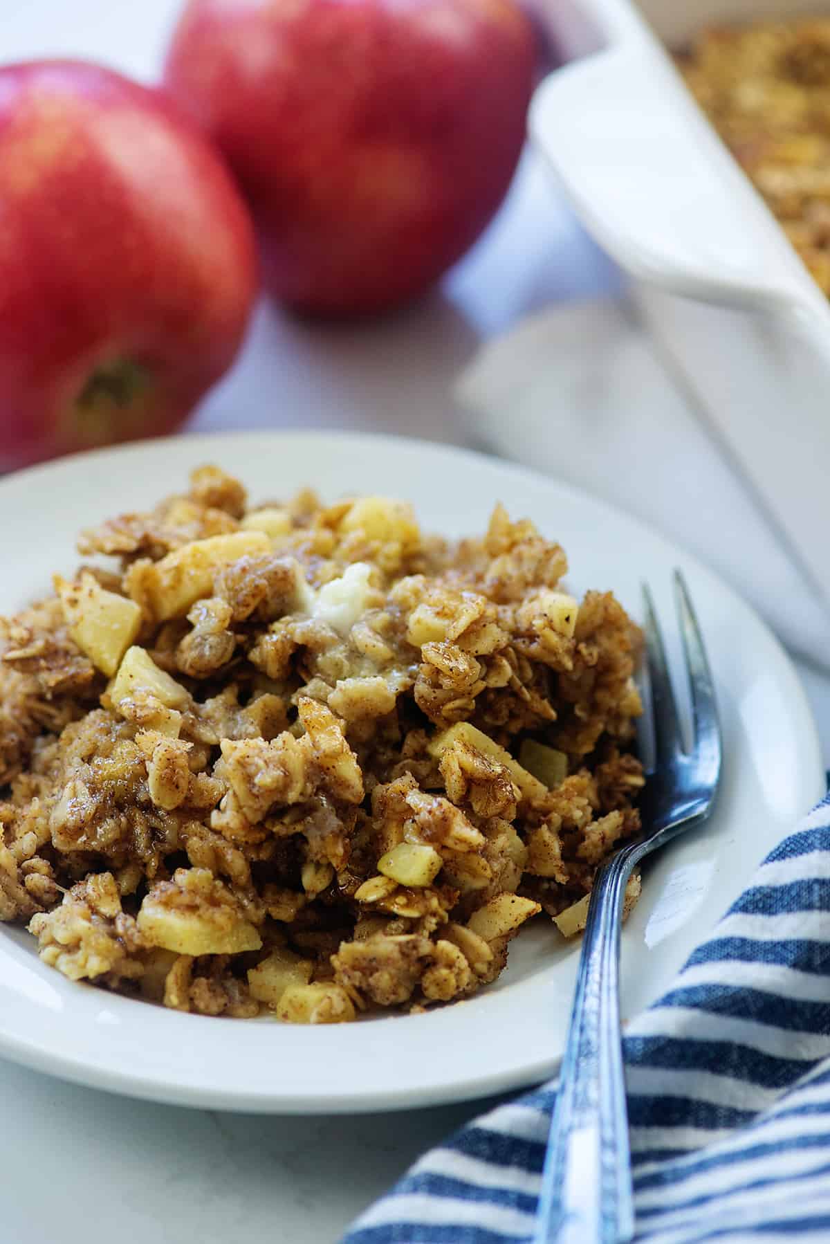 baked apple cinnamon oatmeal recipe on white plate with red apples in background