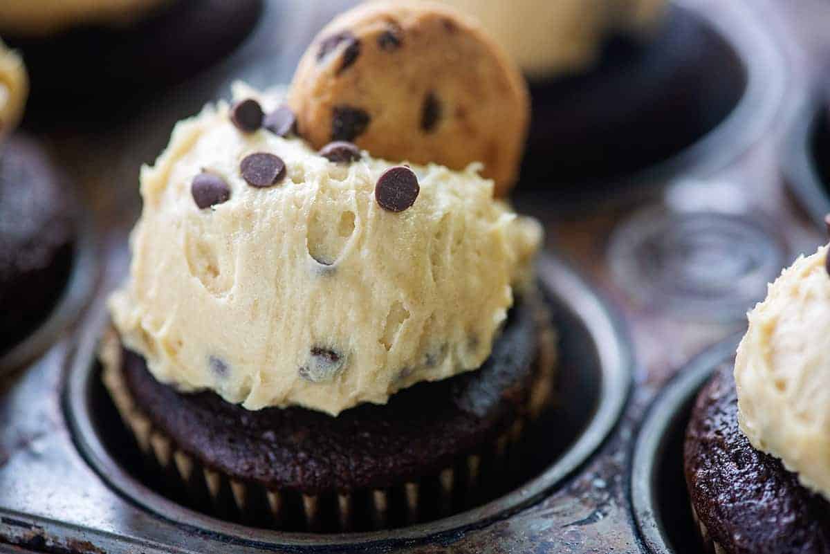 large dollop of frosting topped of with a mini chocolate chip cookie on a cupcake