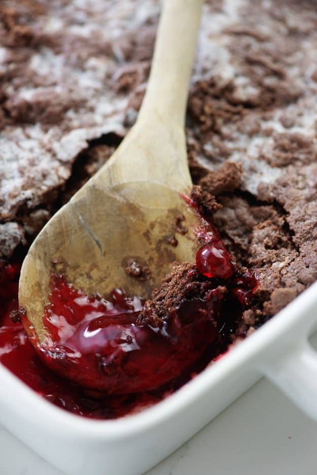 strawberry pie filling and chocolate cake in white baking dish with wooden spoon