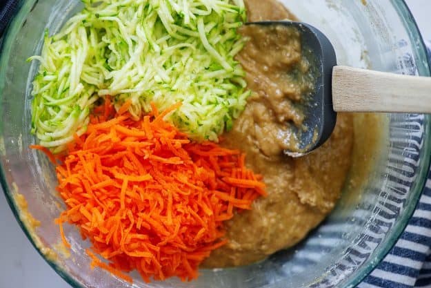 zucchini bread batter with shredded zucchini and carrots in glass mixing bowl