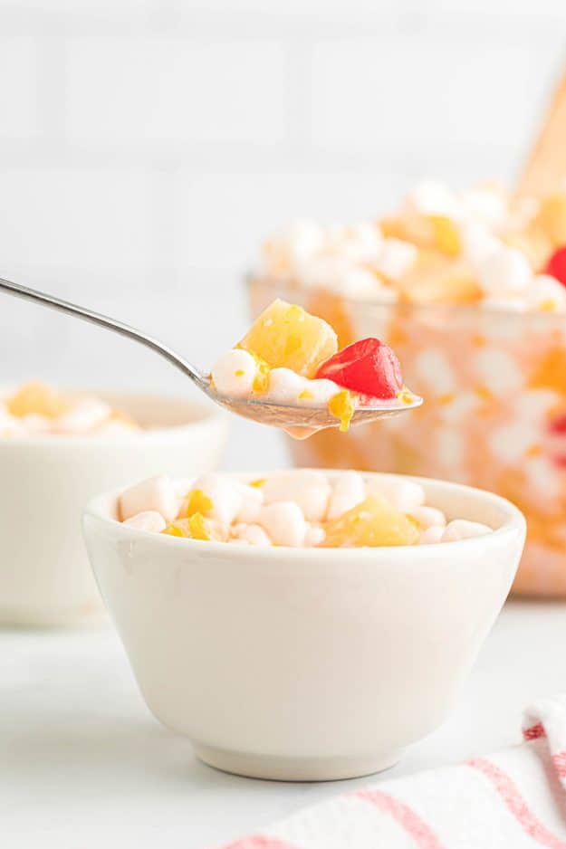 fruit salad with whipped coconut cream in white bowl and on a spoon