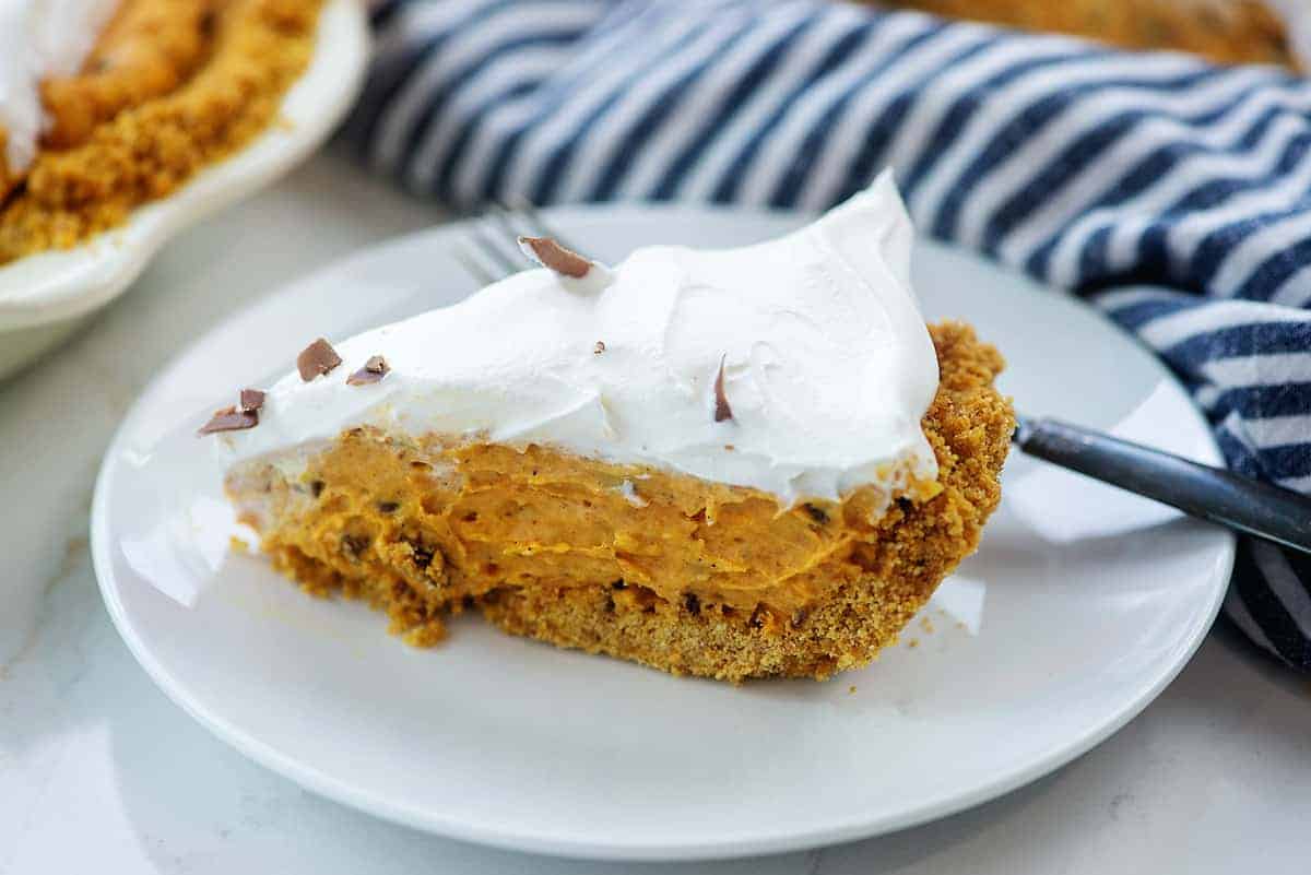 pumpkin pie with chocolate and whipped cream on white plate with blue striped napkin