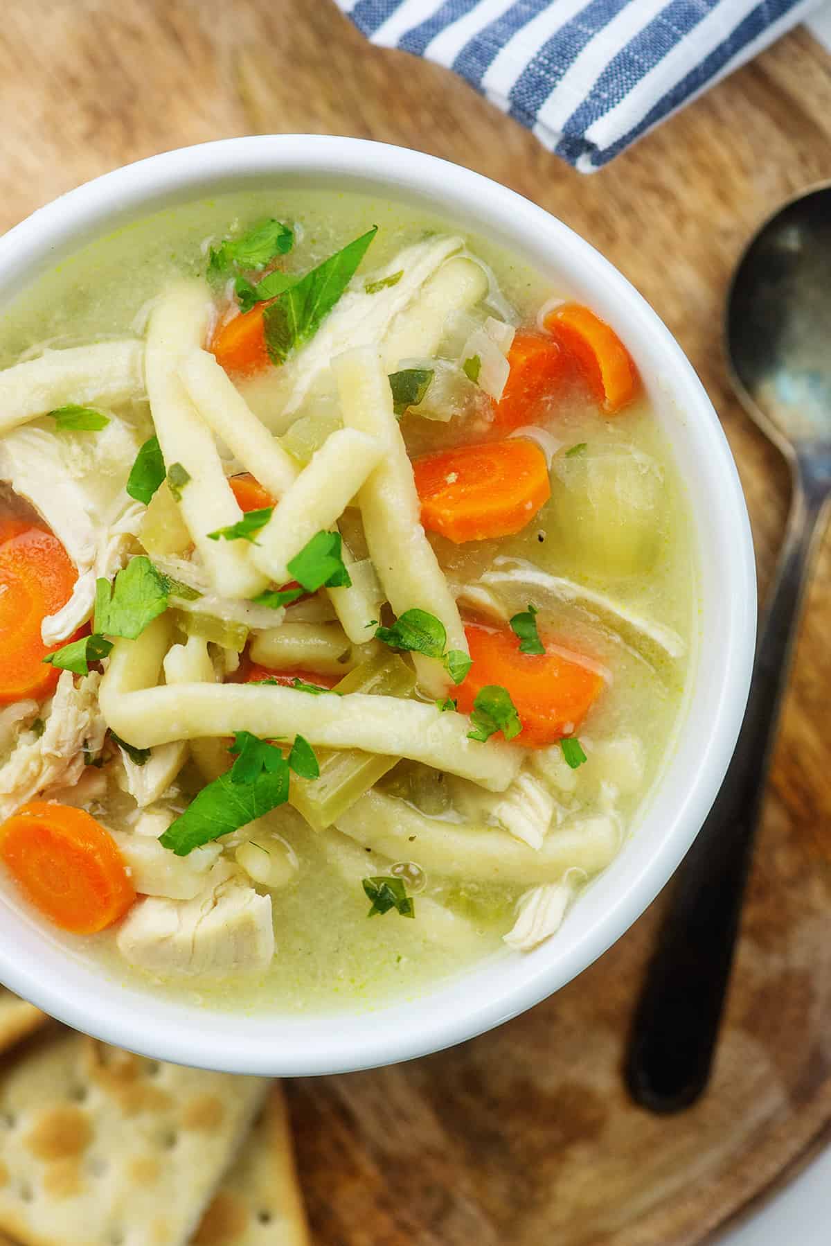 slow cooker chicken noodle soup recipe in white dish surrounded by crackers