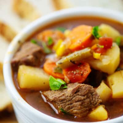 vegetable beef soup recipe in white bowl on wooden board.