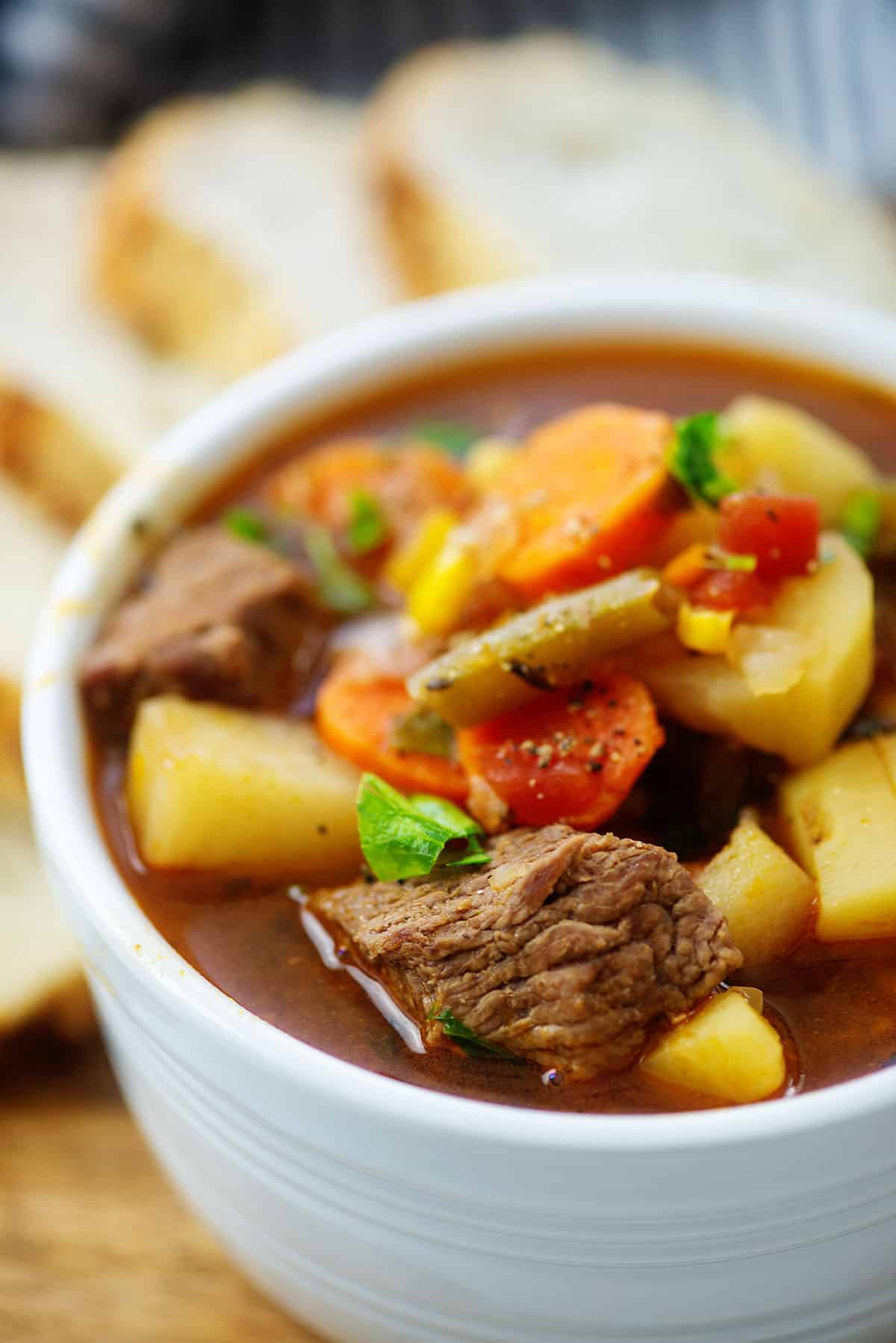 vegetable beef soup recipe in white bowl on wooden board.