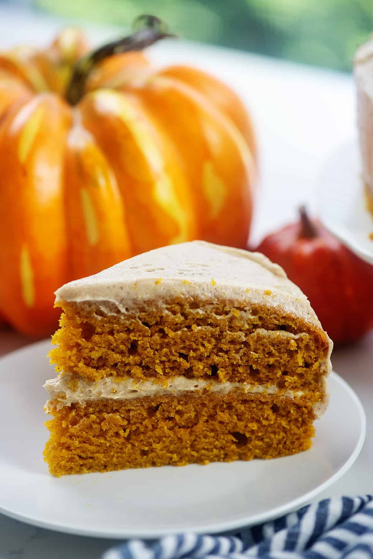 frosted pumpkin layer cake on white plate with pumpkins in the background.
