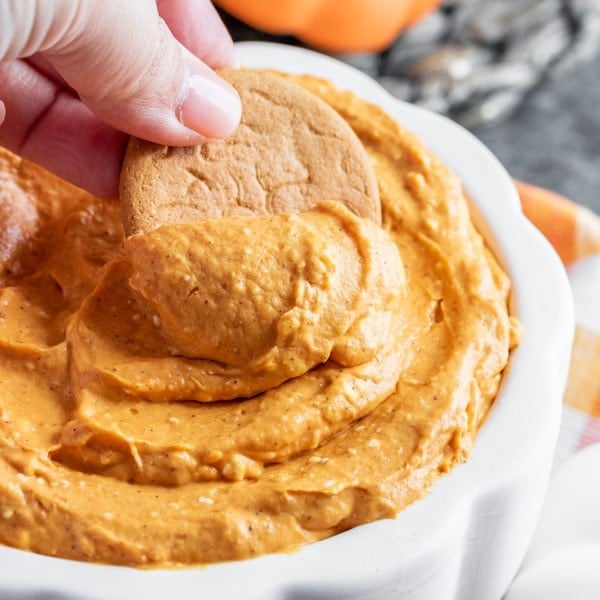 person dipping a cookie in pumpkin dip.
