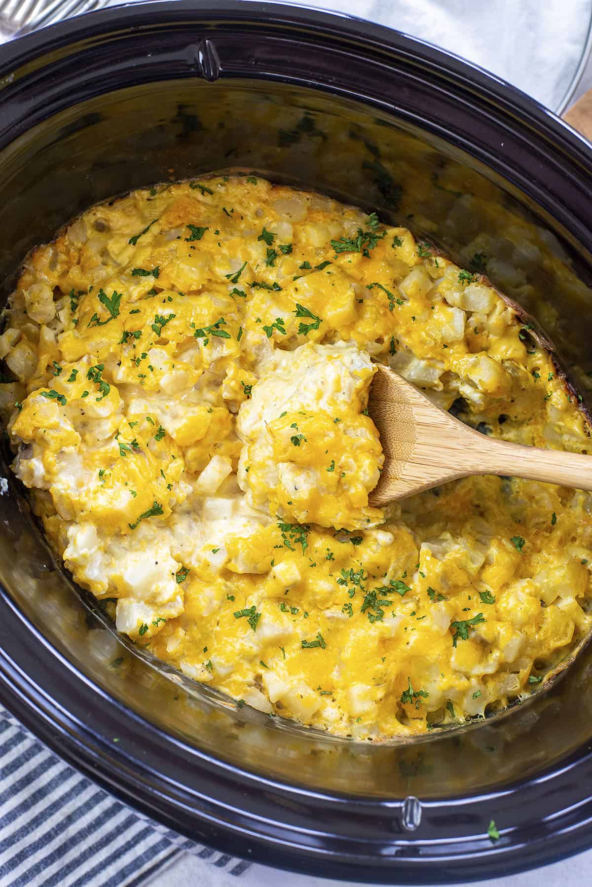 cheesy crockpot hashbrown casserole with wooden spoon.