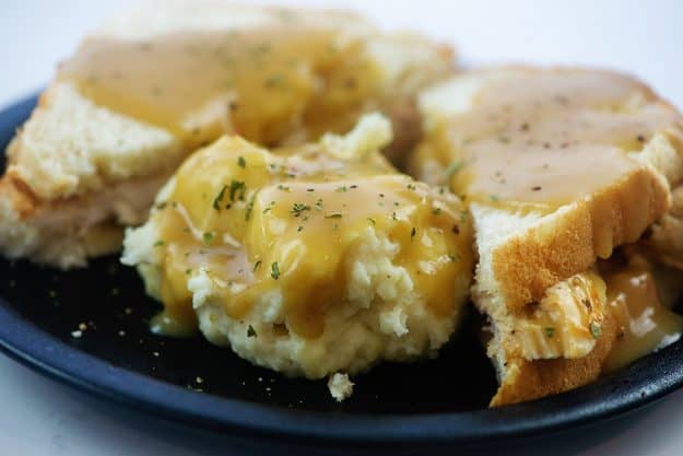 hot turkey sandwich and mashed potatoes topped with gravy on black plate.