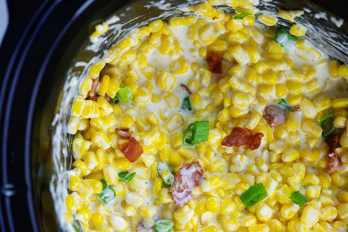 creamed corn in crockpot topped with bacon and green onions.