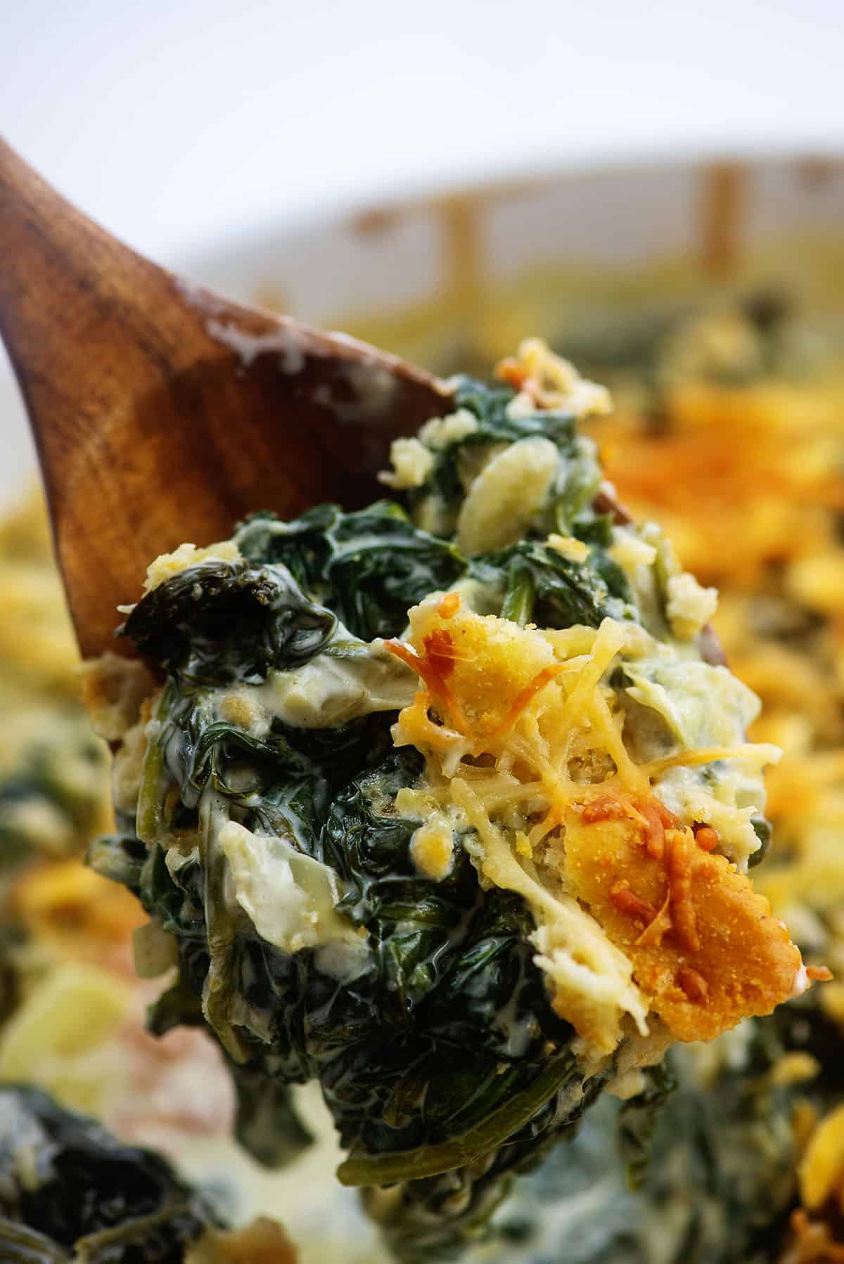 cheesy spinach casserole on wooden spoon.