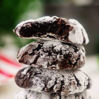 stack of chocolate crinkle cookies in front of Christmas tree.