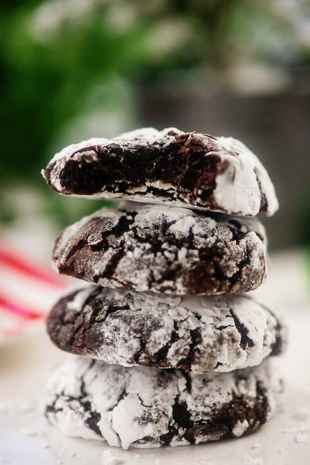 stack of chocolate crinkle cookies in front of Christmas tree.