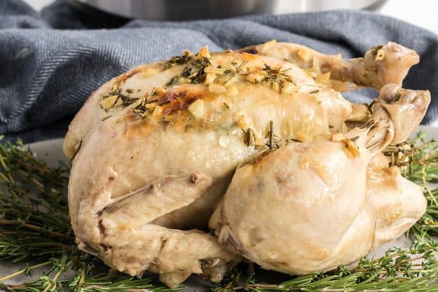 whole chicken cooked in a pressure cooker on a bed of herbs.
