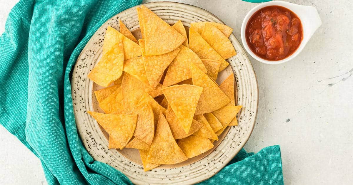 Top down view of air fryer tortilla chips on a plate next to a bowl of salsa.