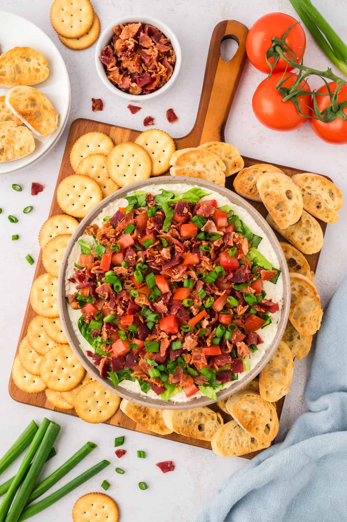 Overhead view of BLT dip recipe on wooden board surrounded by crackers.