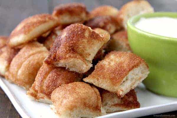 Close up of cinnamon breadstick bites on a tray next to a bowl of frosting for dipping.