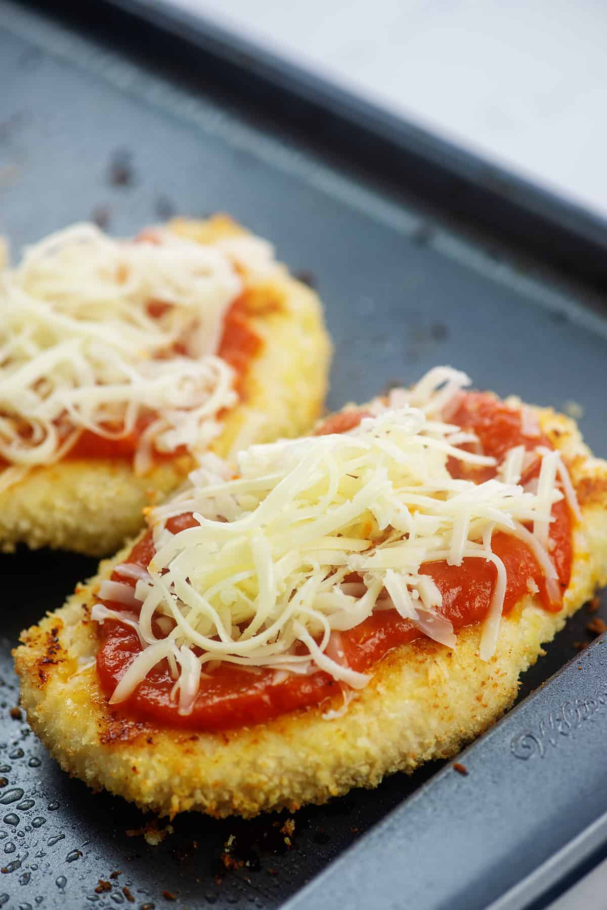chicken breasts topped with marinara and cheese on sheet pan.