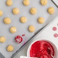 cookie dough balls being dunked in red candy coating.