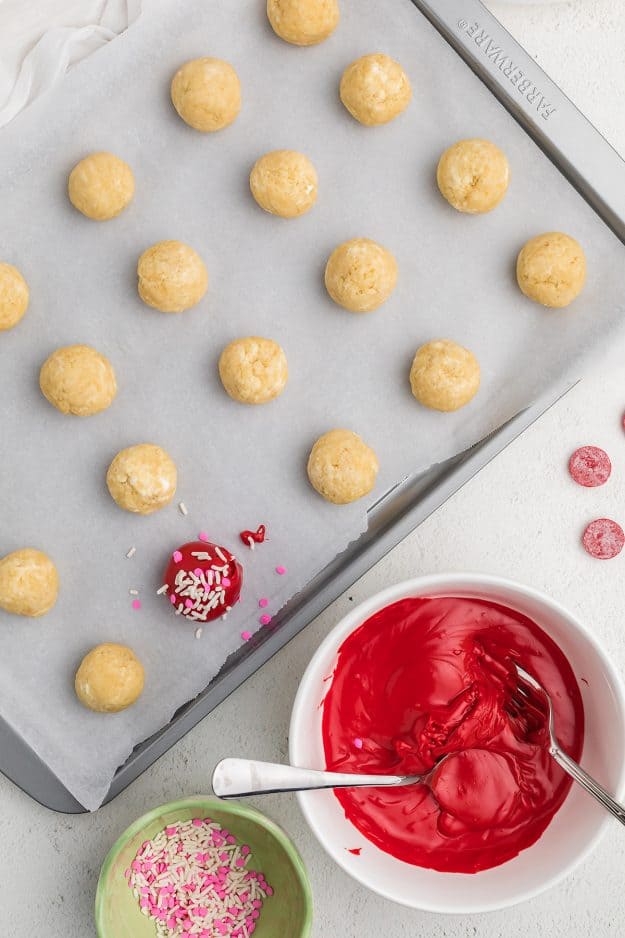 cookie dough balls being dunked in red candy coating.