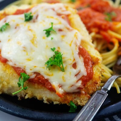 close up of chicken parmesan on black plate.