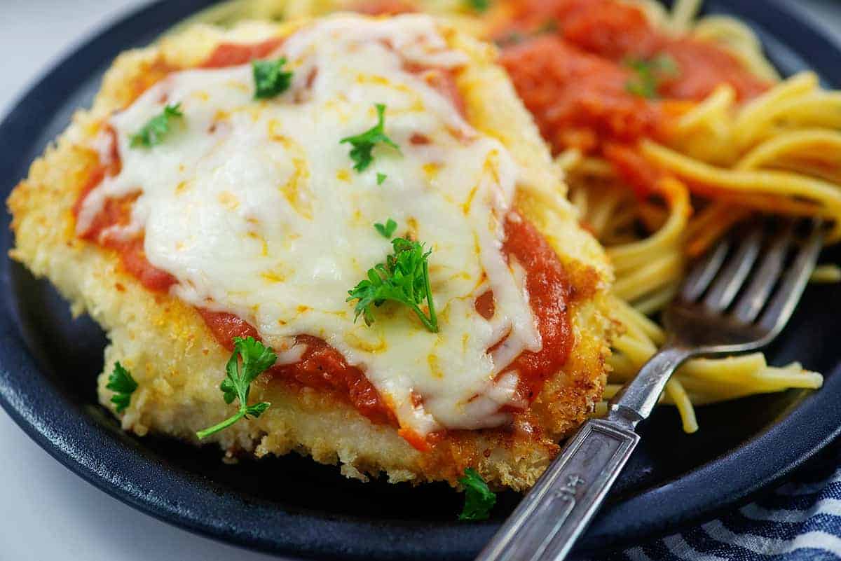 close up of chicken parmesan on black plate.