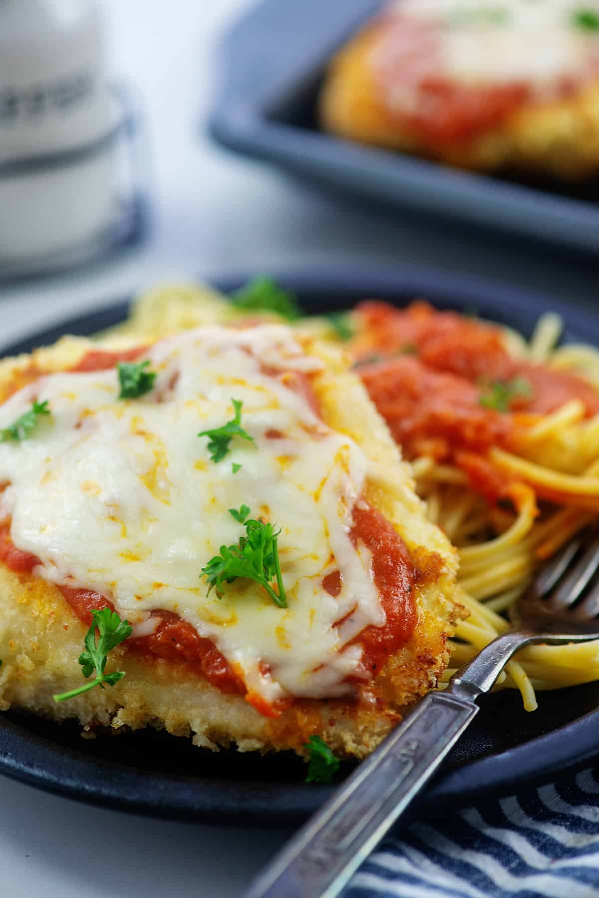 black plate topped with baked chicken parmesan and pile of pasta.
