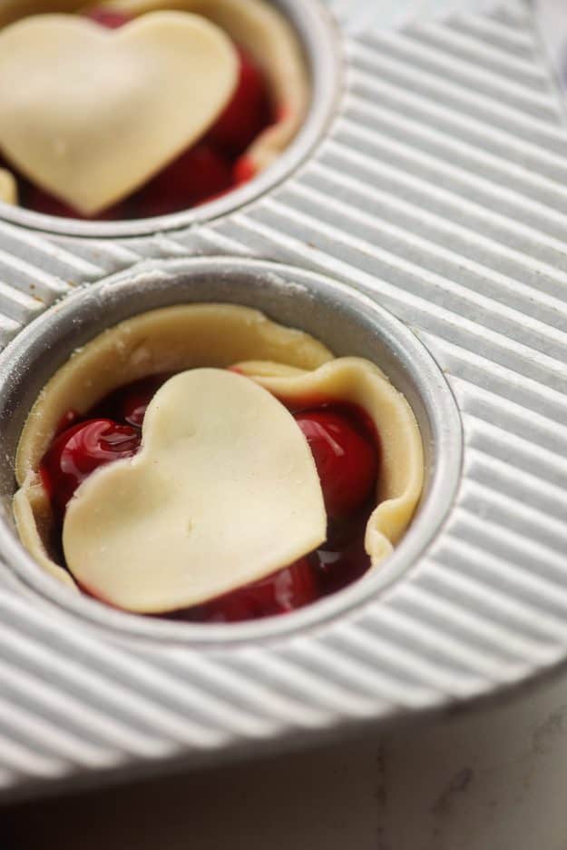 mini pies filled with cherry pie filling and topped with heart shaped crust.