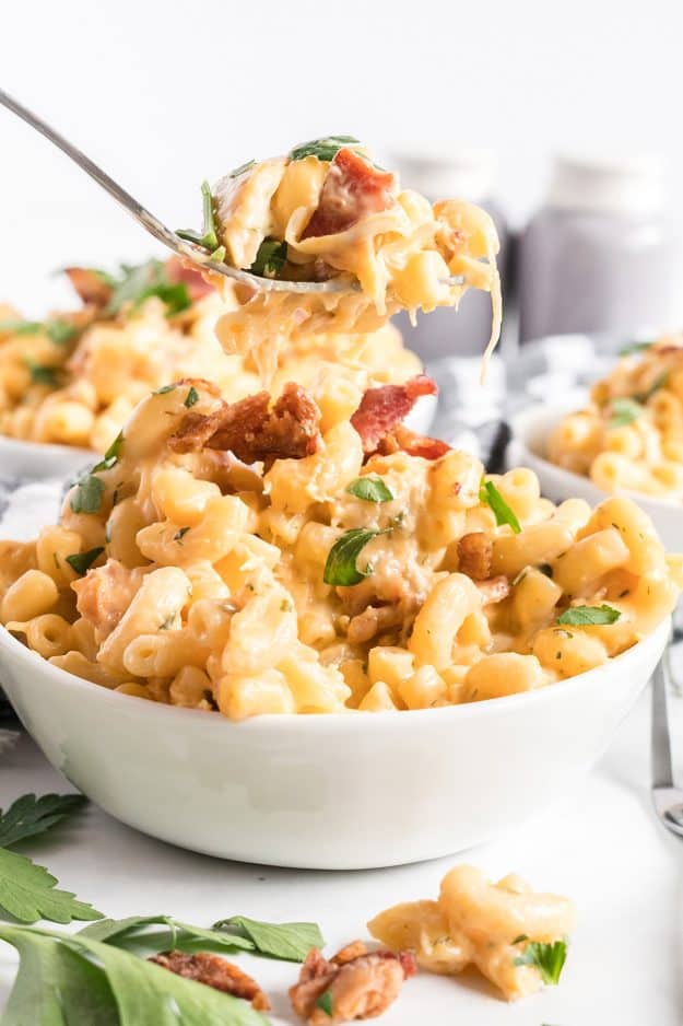 A fork scooping chicken bacon ranch mac & cheese from a white bowl.