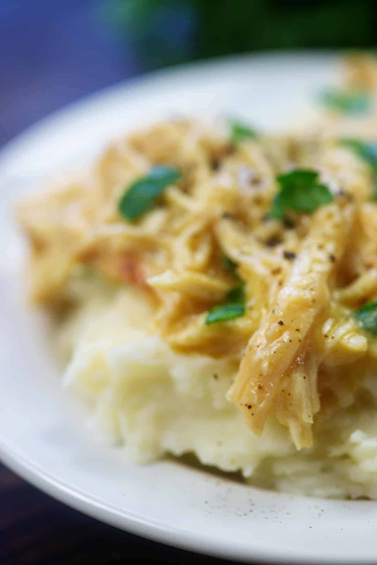 Pile of mashed potatoes on white plate topped with chicken and gravy.