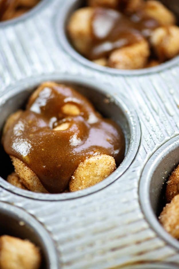 muffin tin full of monkey bread pieces topped off with caramel sauce.