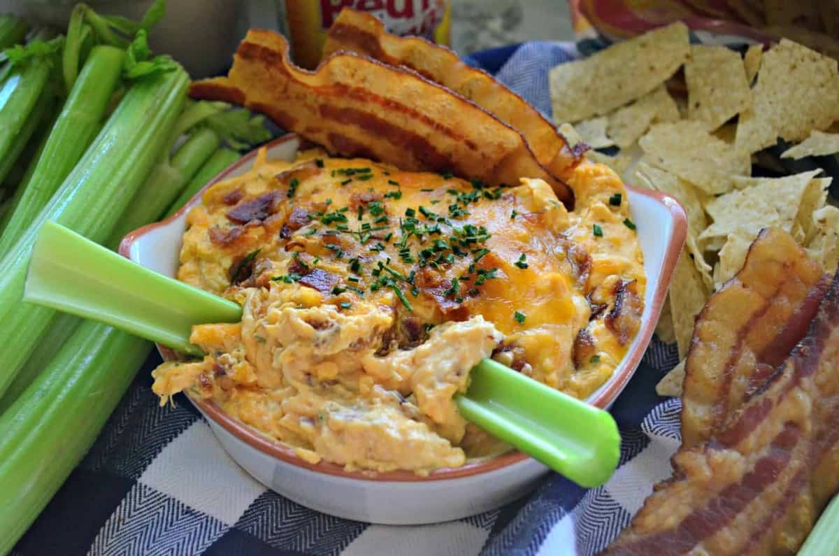 Bacon chive buffalo chicken dip in a bowl with pieces of celery and slices of bacon.
