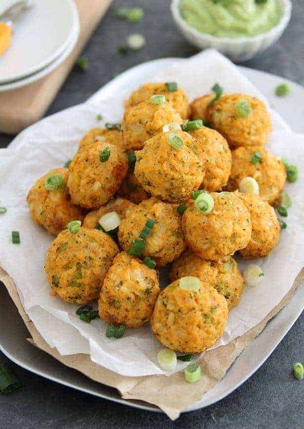 Buffalo chicken cheddar bites with green onion piled on a paper plate.