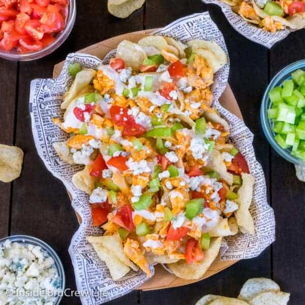 A top down view of buffalo chicken chips in a paper basket next to bowls of toppings.